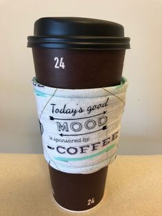 a coffee cup sitting on top of a counter next to a paper bag with the words today's good mood written on it