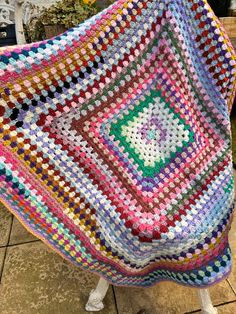 a crocheted blanket sitting on top of a white chair next to a potted plant