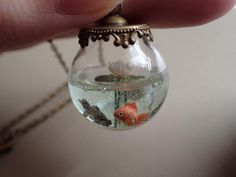 a tiny glass ball with goldfish in it being held by someone's hand