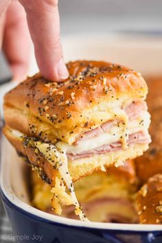 someone is holding a ham and cheese sandwich in a blue bowl with bread rolls on the side