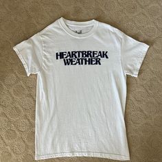 a white t - shirt with the words heart break weather on it sitting on a bed