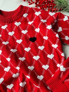 a red sweater with white hearts on it next to a sprig of rosemary