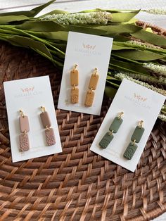 three pairs of earrings sitting on top of a wicker basket next to some flowers