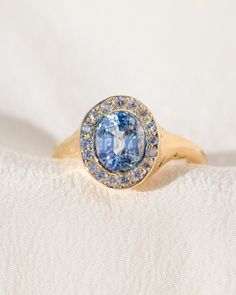 a ring with a blue stone surrounded by small diamonds on a white cloth, close - up