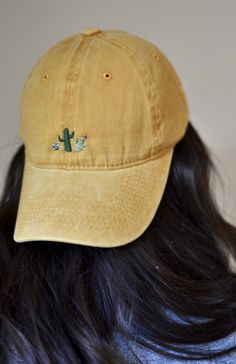 the back of a woman's head wearing a yellow hat with cactus embroidered on it