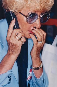 an older woman talking on a cell phone while wearing sunglasses and a blue suit jacket