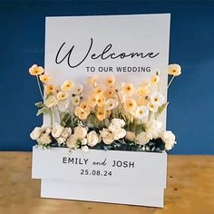 a welcome card with flowers on it sitting on a wooden table in front of a blue wall