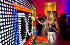 two women standing next to each other in front of an array of colored glasses on display