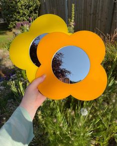 a person holding up a flower shaped mirror in front of a fenced area with flowers