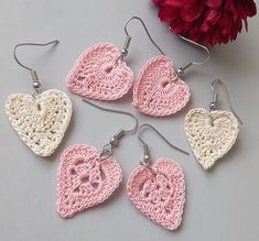 four crocheted heart shaped earrings are shown next to a red flower on a gray surface