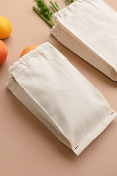 two white bags sitting on top of a table next to fruits and vegetables