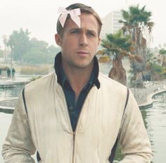 a man with a pink bow on his head standing in front of a pond and palm trees