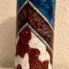 a blue vase with brown and white designs on it's sides, sitting against a wall