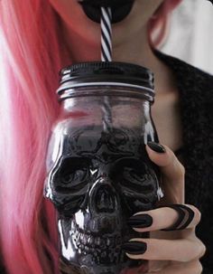 a woman with pink hair holding a mason jar filled with black liquid and a skull