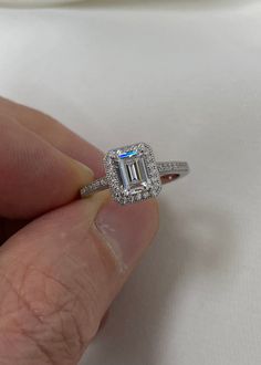 a woman's hand holding an engagement ring with a large emerald stone in the center