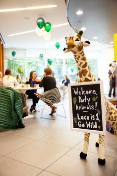 a giraffe holding a sign that says welcome party animals