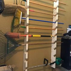 a wall mounted rack with brooms and rakes on it