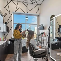 a woman is getting her hair done in a room with large windows and black chairs