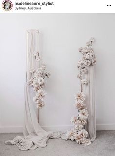 two tall white flowers are next to each other on the floor in front of a wall