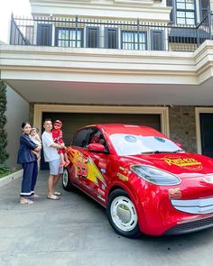 three people standing in front of a red car