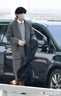 a man wearing a face mask walking next to a car