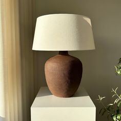 a large brown vase sitting on top of a white block next to a lamp shade