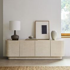 a white sideboard with two vases and a framed photograph on it in front of a window