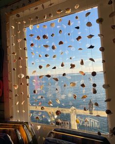 a window with sea shells hanging from it's side and the ocean in the background