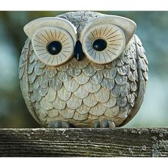 an owl figurine sitting on top of a wooden fence post with its eyes wide open