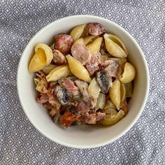 a white bowl filled with pasta and meat on top of a blue table cloth next to a fork