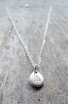 a silver necklace with a small tree on the front and bottom, sitting on a wooden surface