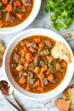 two bowls of stew with bread and parsley on the side, one bowl is filled with soup