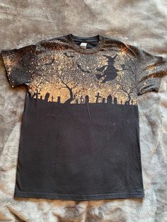 a black t - shirt with gold glitter on the front and graveyard silhouettes on the back