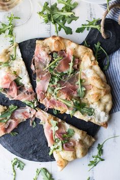 two slices of pizza sitting on top of a black plate next to a glass of wine