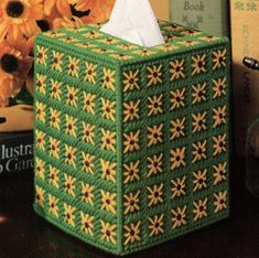 a green tissue box sitting on top of a wooden table next to books and flowers