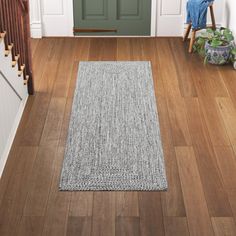 a wooden floor in front of a green door with a gray rug on the ground