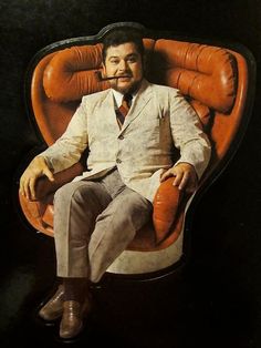 a man sitting in an orange chair wearing a suit and tie