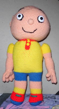 a crocheted doll with big eyes and a yellow shirt on top of a bed