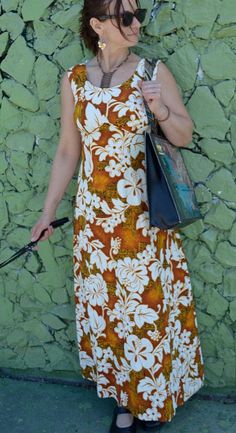 a woman standing in front of a green wall holding a black bag and wearing sunglasses