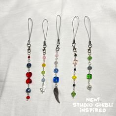 four different colored beads hanging from silver earwires on a white background with the words new studio ghibli inspired written below them