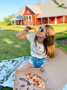 a woman sitting on the grass drinking from a box with a slice of pizza in it