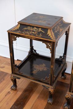 two black and gold painted side tables on wooden floor with white wall in the background