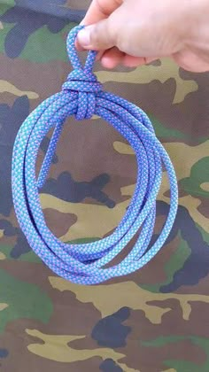 a hand holding a blue rope in front of camo print fabric with the string attached to it