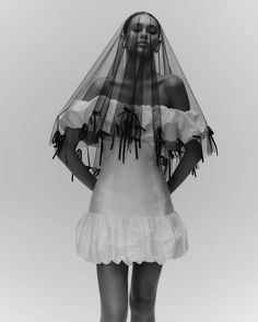 black and white photograph of a woman wearing a veil over her head, standing in front of the camera