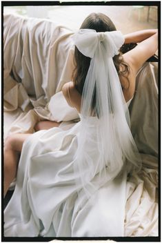 a woman in a wedding dress sitting on a bed with her veil over her head