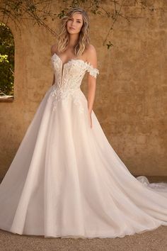 a woman in a white wedding dress standing next to a stone wall with vines on it