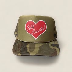 Looking for a stylish and cool trucker hat for Valentine's Day or just to complete your casual look? Look no further than the Cold Hearted Trucker Hat! This trendy foam mesh trucker hat comes in a cool camo, and features a bold red heart design on the front that is sure to turn heads. Whether you're hanging out on the beach, running errands around town, or just lounging at home, this hat is the perfect accessory to add some flair to your outfit. The adjustable snapback closure ensures a comfortable fit for all head sizes, while the breathable mesh fabric keeps you cool and comfortable all day long. So why wait? Add the Cold Hearted Trucker Hat to your collection today and show off your unique style! Trendy Winter Trucker Hat, Trendy Winter Trucker Hat Snapback, Trendy Winter Trucker Snapback Hat, Winter Trucker Hat With Curved Brim, Red Heart Design, Camo Trucker Hat, Beach Running, Custom Trucker Hats, Cold Hearted