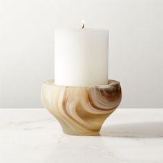 a white candle sitting on top of a marbled table next to a white wall