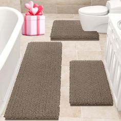 three bathroom rugs on the floor in front of a bathtub with a gift box