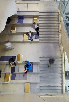 three people sitting on benches in the middle of a building with stairs leading up to them